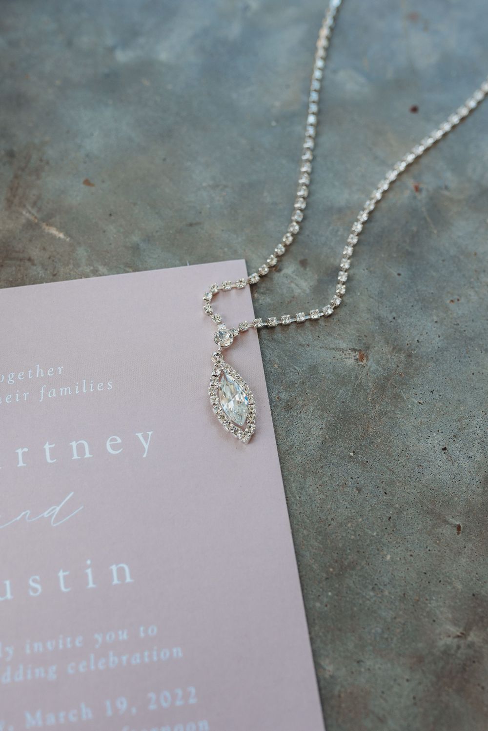 Delicate crystal necklace laying across pink wedding invitation.