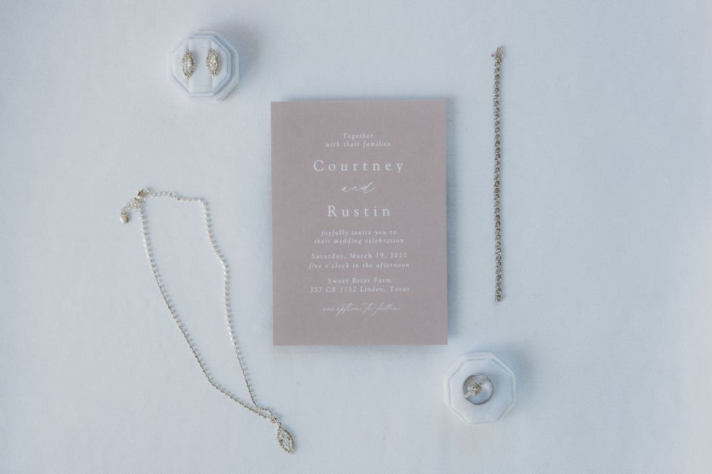 Wedding invitation and jewelry details arranged on white surface with minimalist styling.