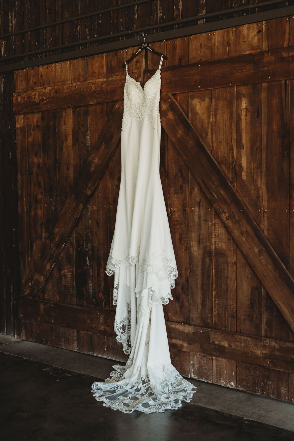 Elegant white wedding dress with lace trim hanging against rustic wooden barn doors.