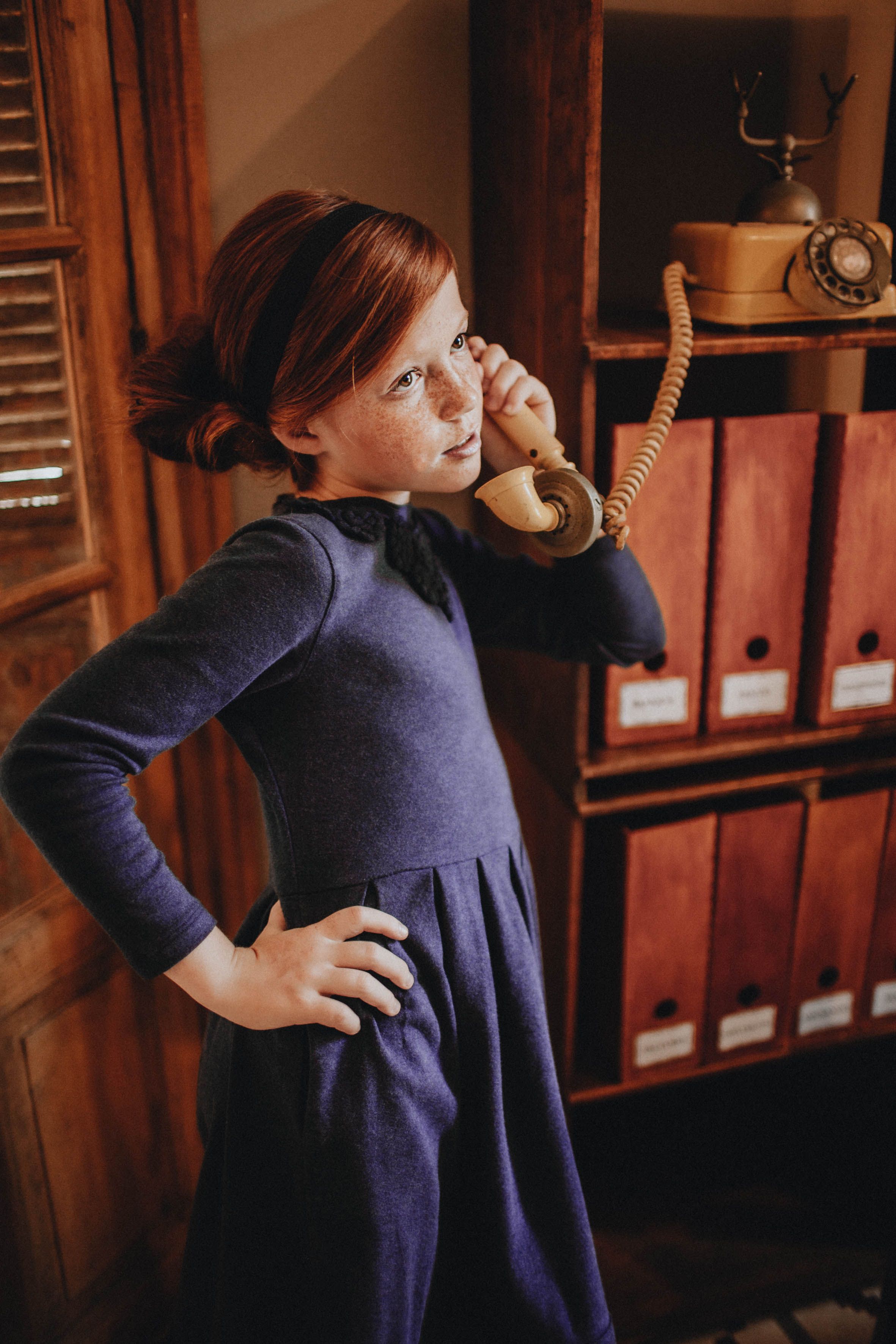 Natural light portrait of a red-haired child responding to a vintage phone, evoking curiosity, charm, and retro atmosphere.