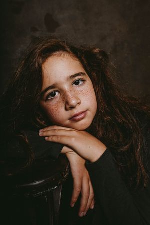 Studio portrait of a red-haired, freckled girl dressed in black, captured with dramatic studio lighting highlighting natural beauty