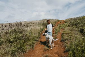 Child wearing a vintage t-shirt petting a dog on a red hill, captured in natural light with a nostalgic outdoor lifestyle vibe.