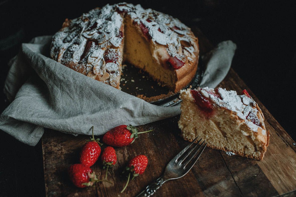 Dark style photography of a strawberry cake with a sliced piece, highlighting dramatic light, texture, and elegant presentation.