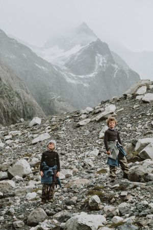 Two children climbing a misty mountain, capturing a nostalgic and adventurous atmosphere, with fog creating a timeless, magical landscape.