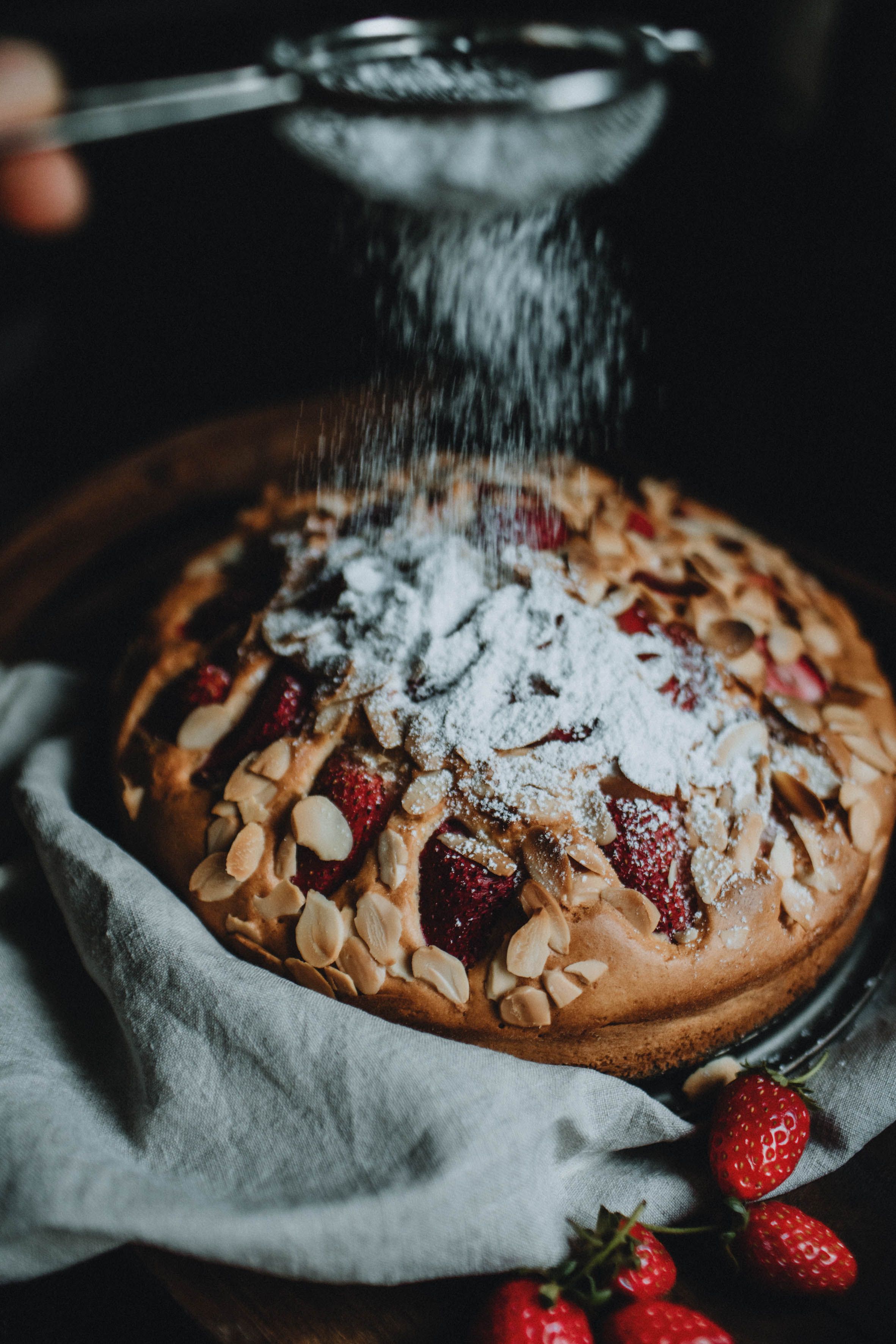 Strawberry cake in dark photography style, dusted with powdered sugar, showcasing moody and elegant dessert photography.