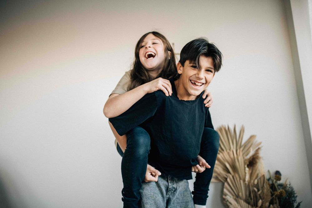 Playful piggyback ride moment captured indoors with decorative pampas grass in background.