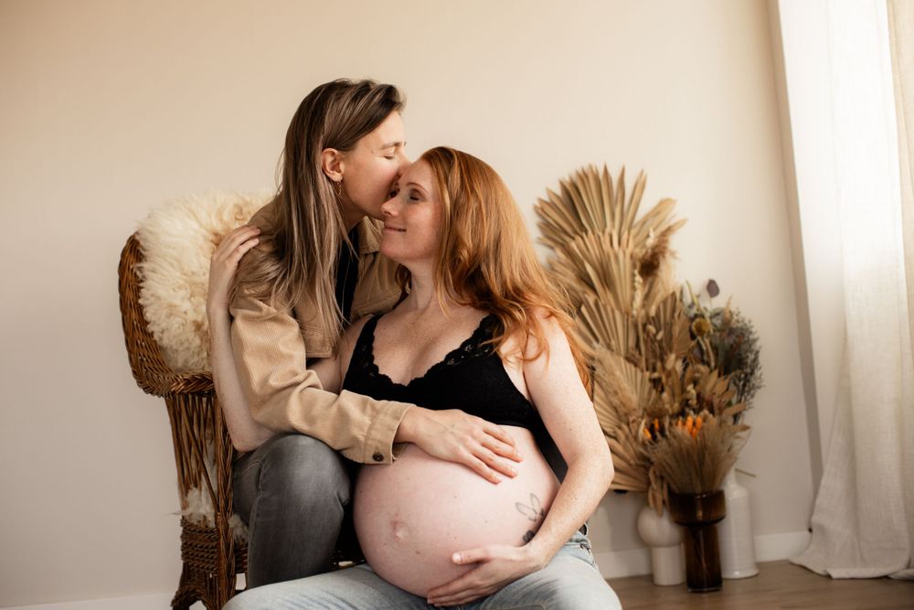 Intimate maternity portrait with couple relaxing in chair with dried pampas grass decor.