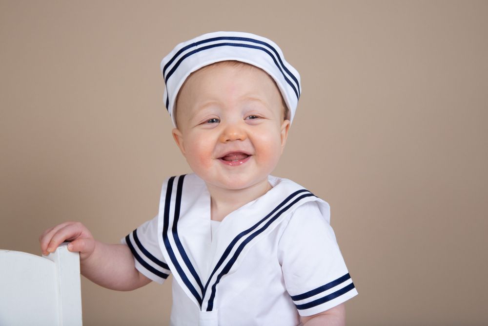 A joyful portrait of a young child wearing a nautical-themed white and navy sailor outfit.