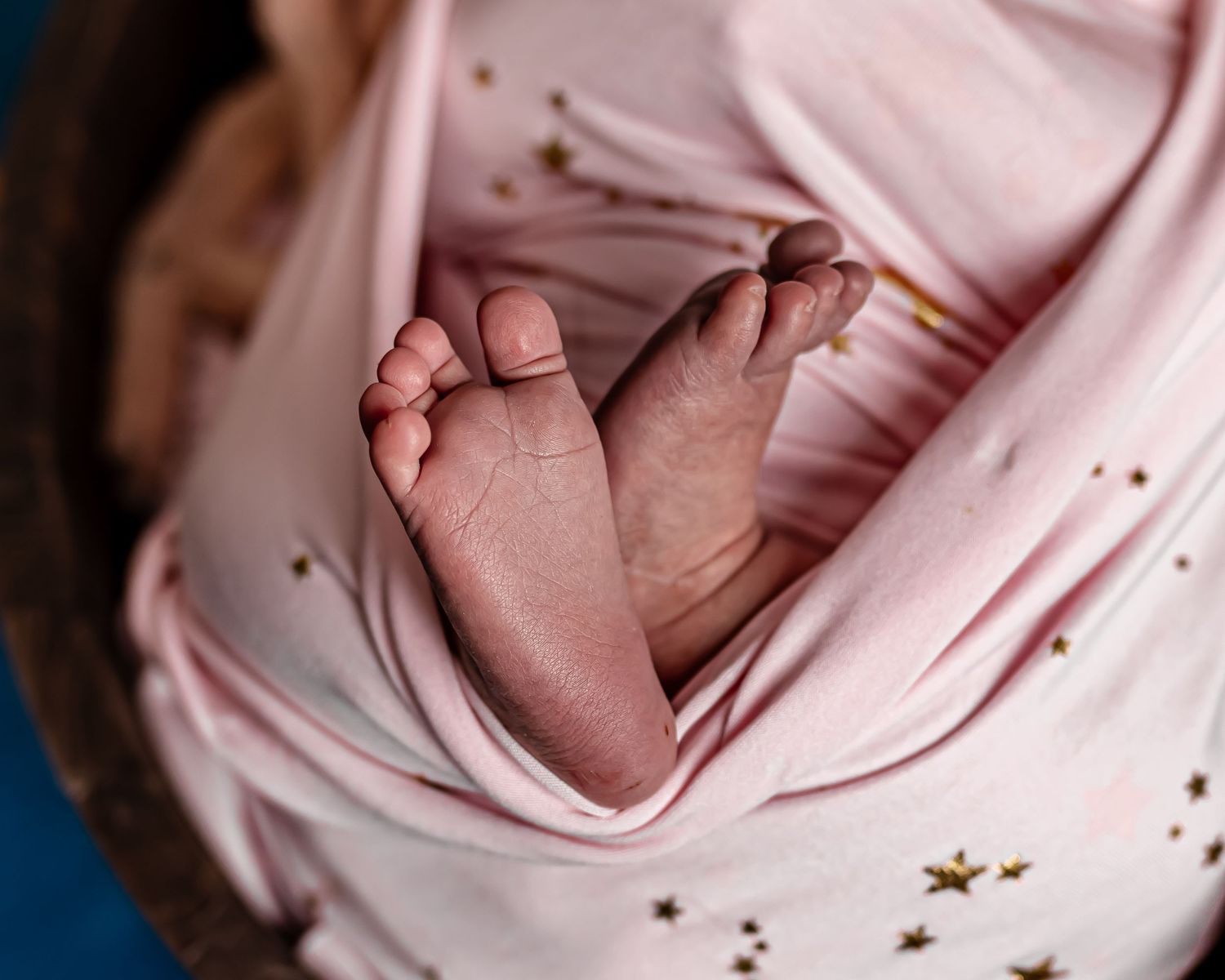 Close-up photo of tiny baby feet against pink fabric with golden star details.