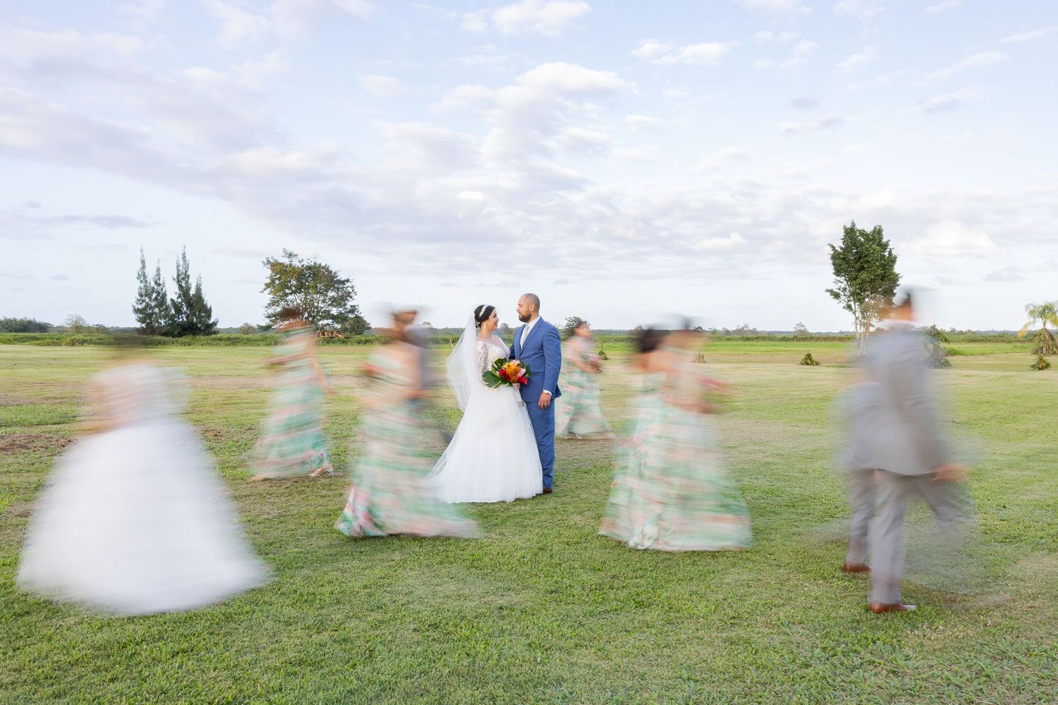 A wedding party walking on a grassy field with blurred figures in the background.