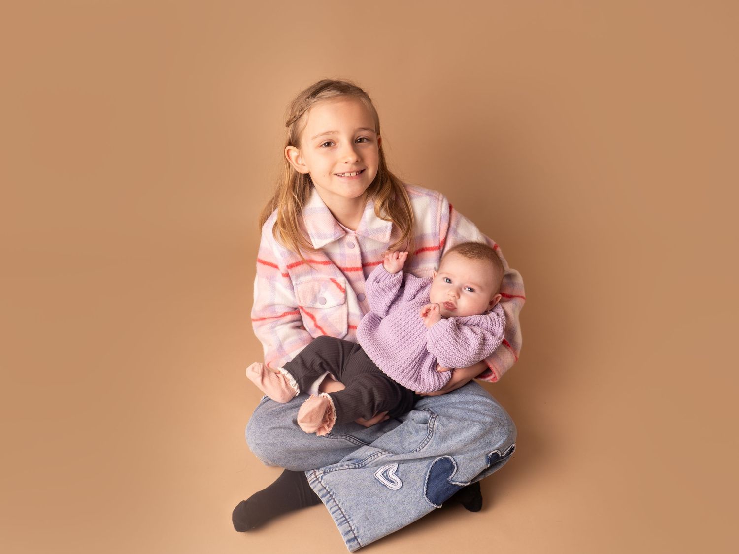 Proud big sister holding new addition to the family small baby in purple jumper for family photoshoot in doncaster.