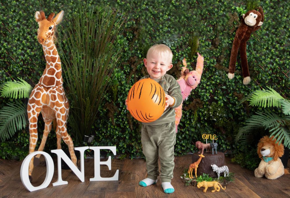 Smiling toddler boy holding a pumpkin at a jungle safari first birthday photo shoot with animal props.