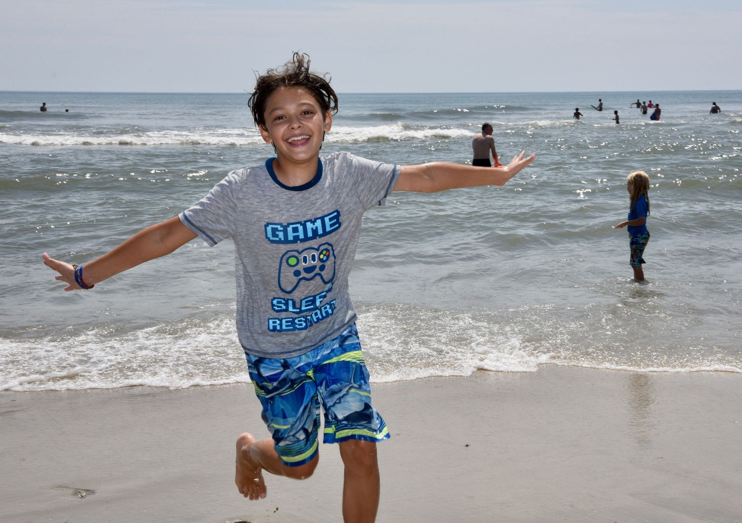 Young child jumps joyfully on beach with ocean waves in background.