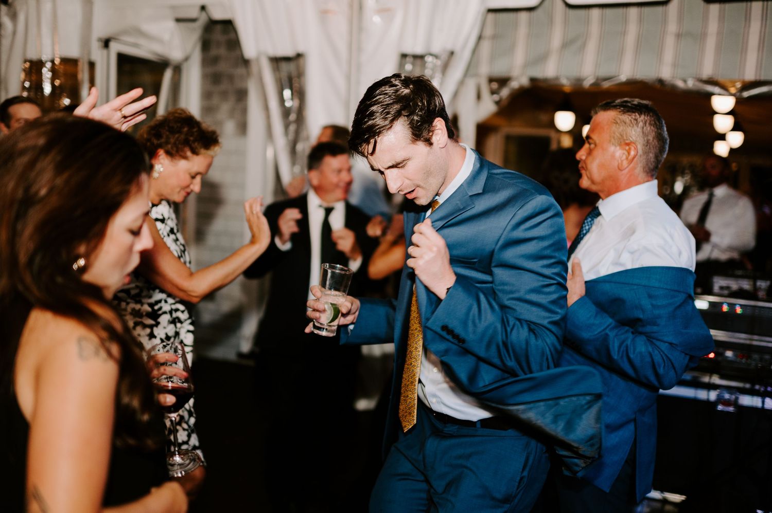 Wedding guests dance and celebrate on a dimly lit dance floor with string lights overhead.