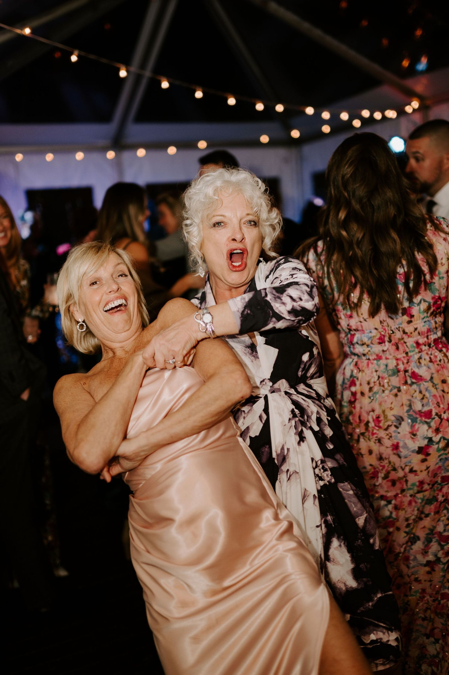Wedding reception dance party with guests in formal attire enjoying themselves under string lights.