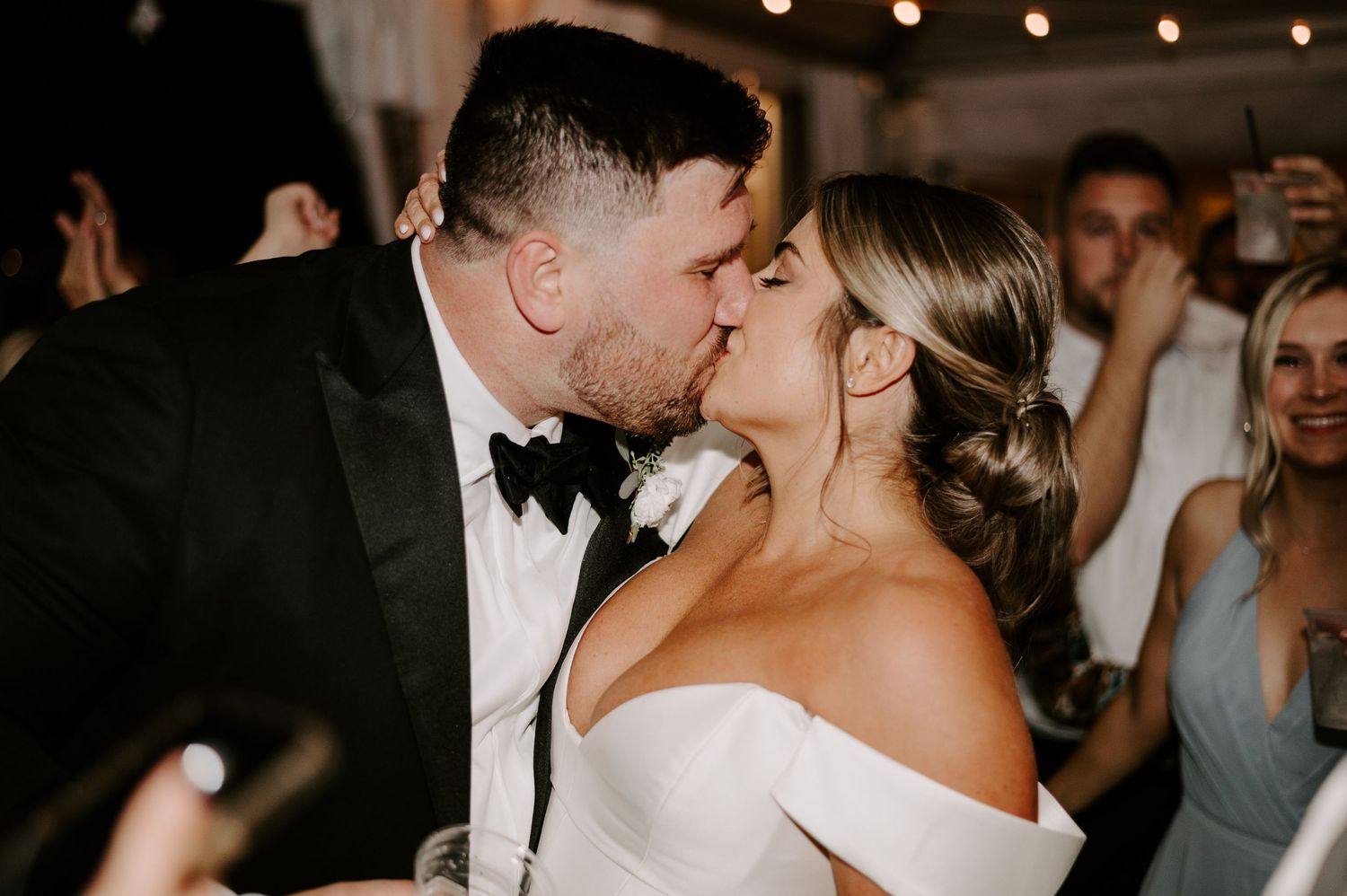 Elegant wedding celebration with guests dancing in a dimly lit venue.