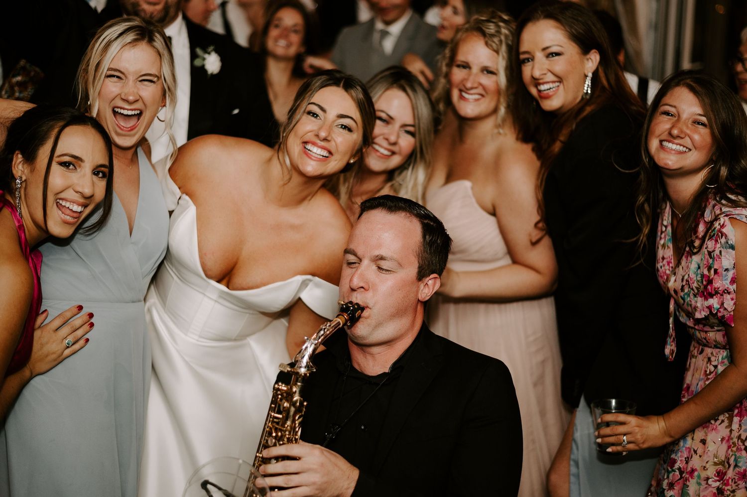 Wedding guests dance and celebrate joyfully at an indoor reception party.