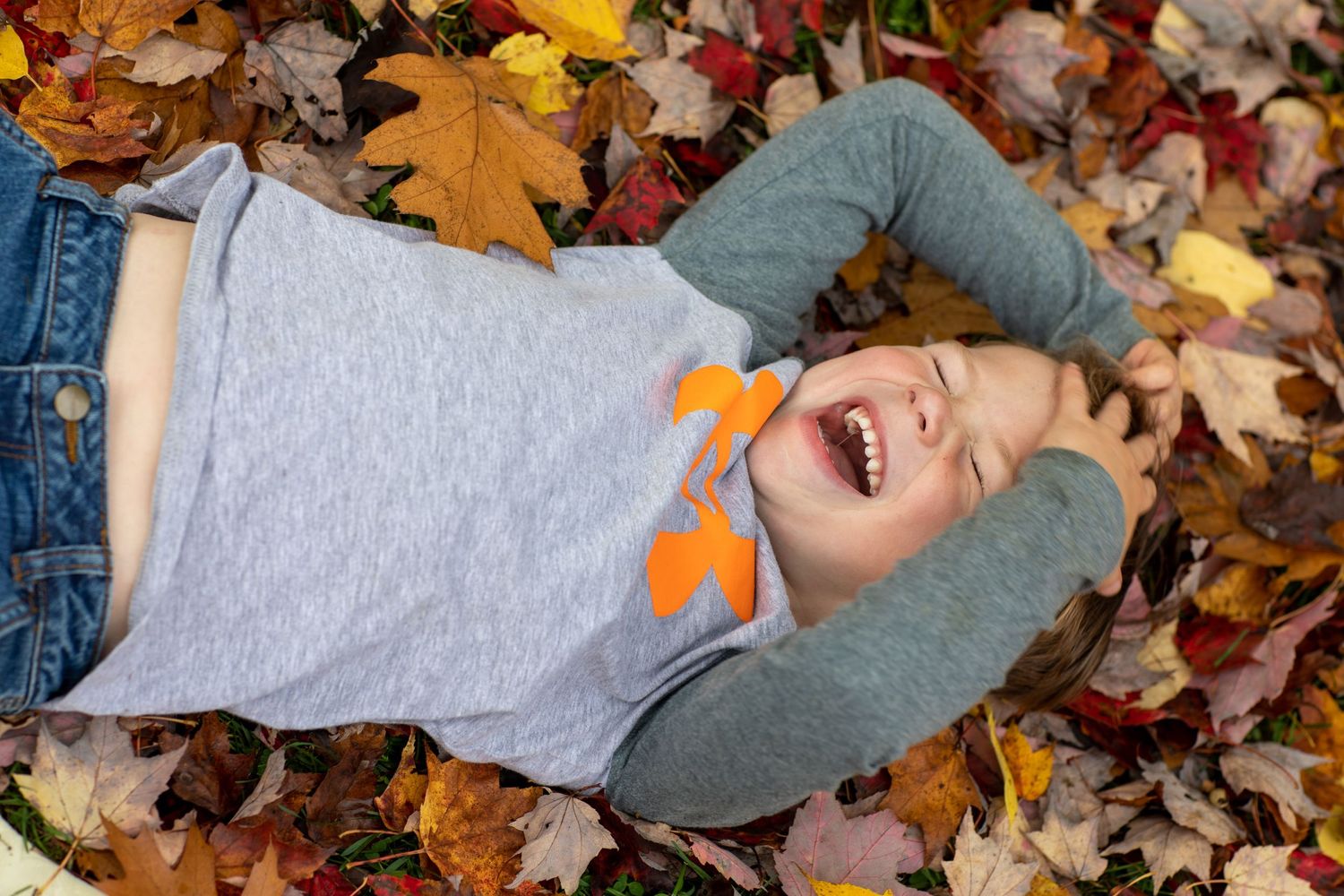 Someone lying in colorful autumn leaves wearing casual clothing.