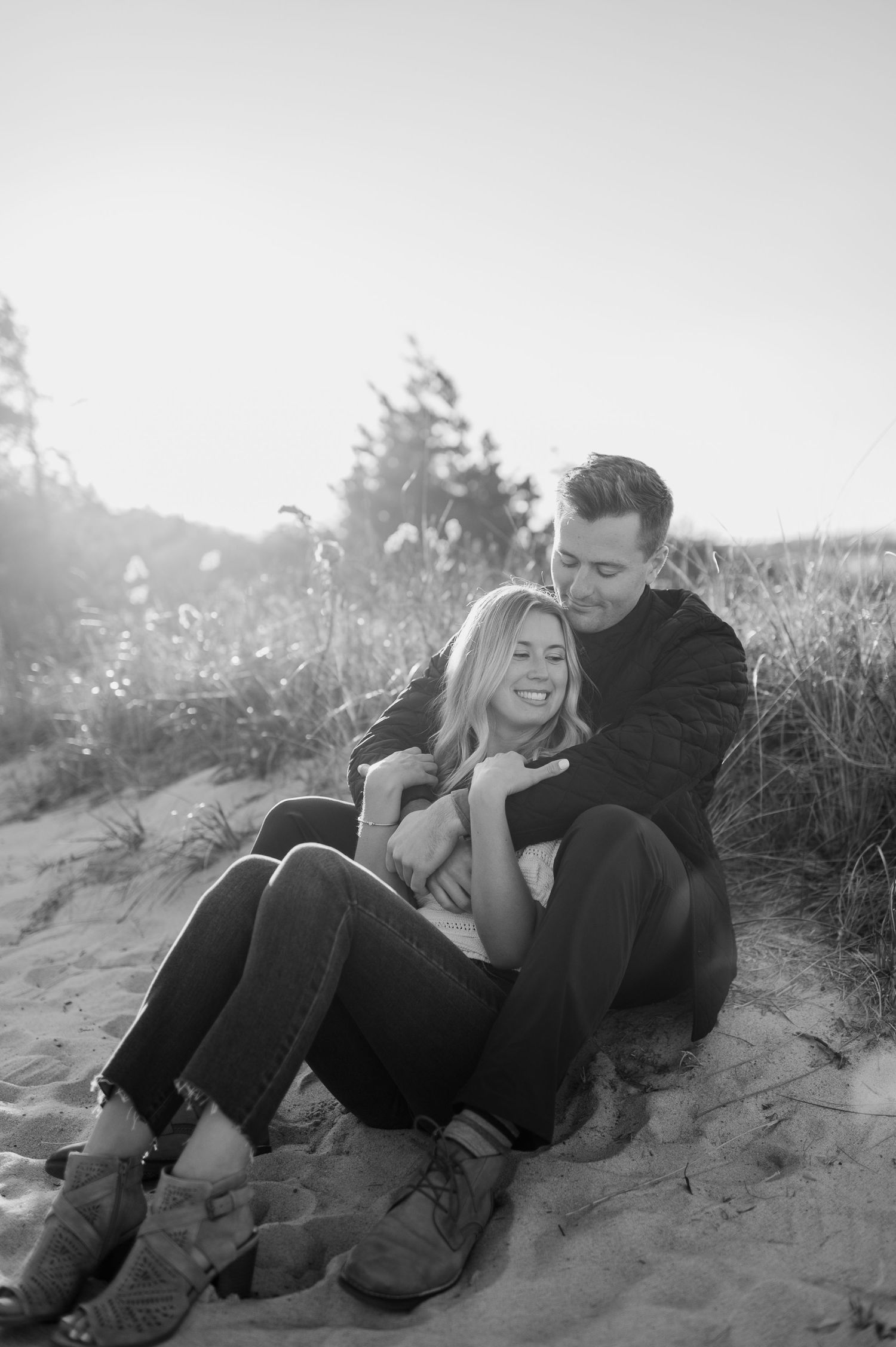 A couple lies together on sandy dunes during a romantic photoshoot at golden hour.