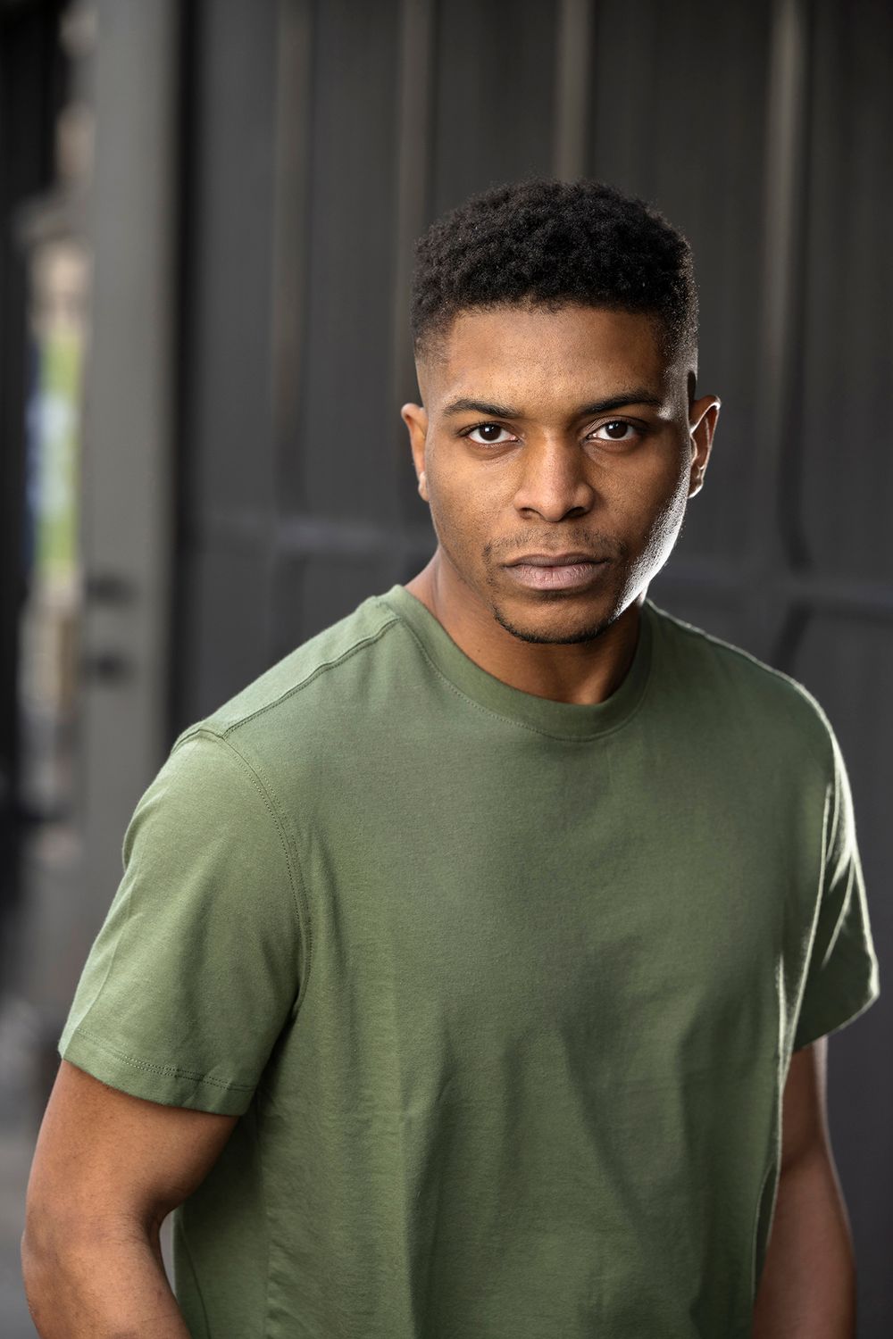 Serious young Black man in a green t-shirt poses for a portrait outdoors.