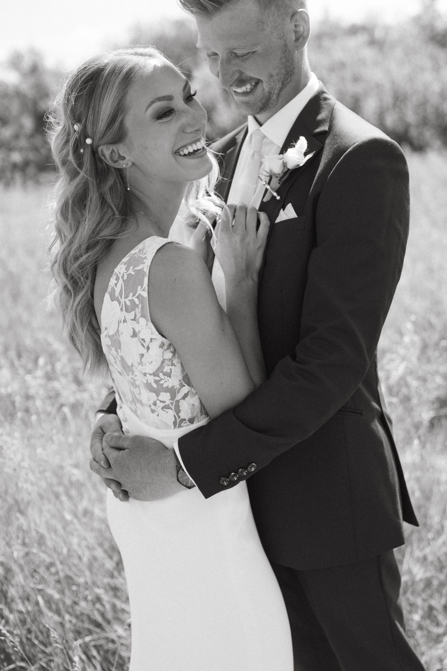 Black and white wedding portrait of newlyweds sharing a joyful moment in a field.