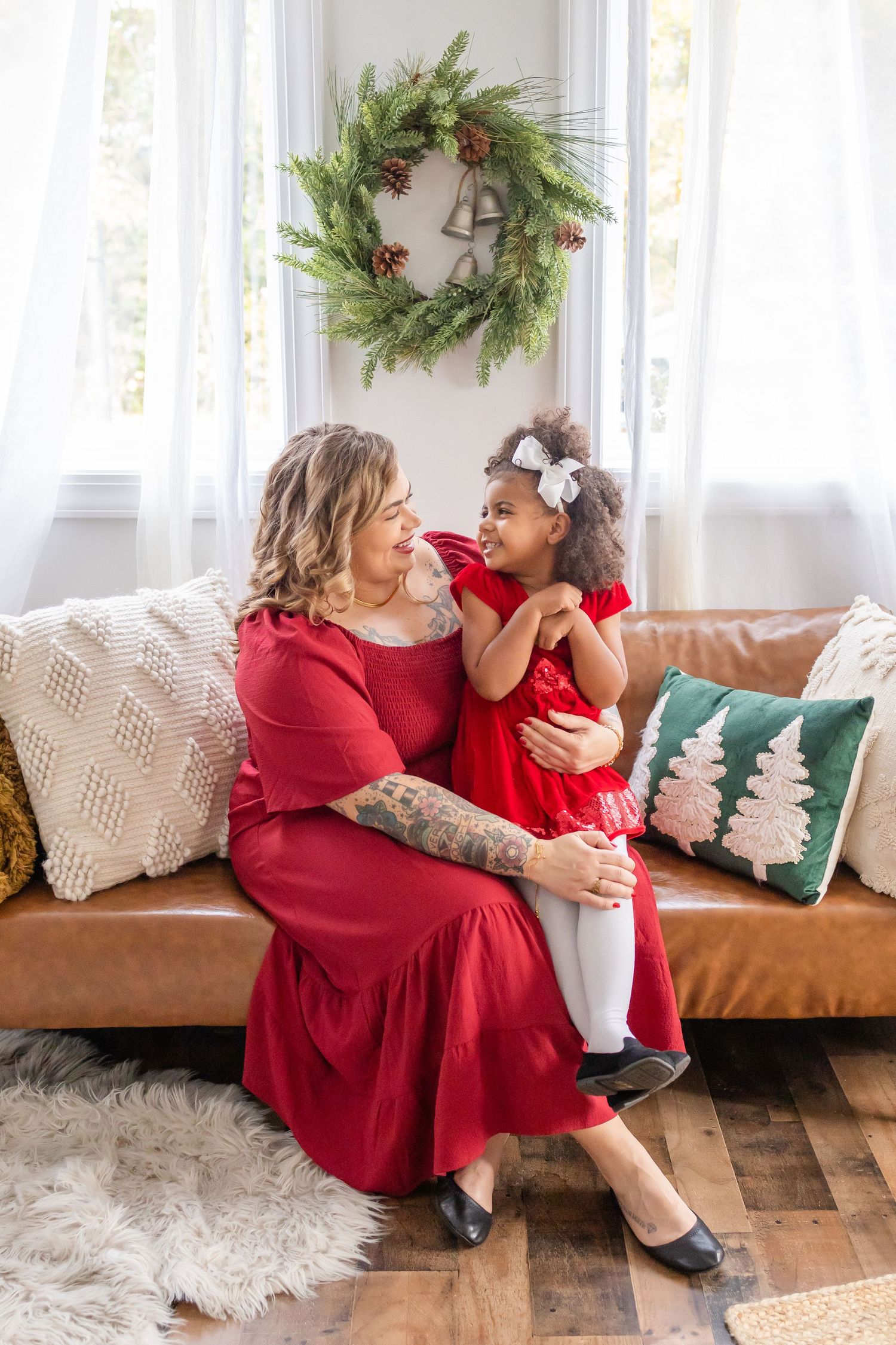 An intimate holiday portrait on a brown leather couch with a Christmas wreath on the wall.