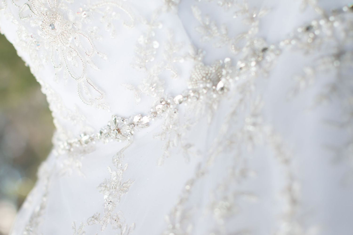 Close-up detail of delicate beading and lace on white wedding dress fabric.