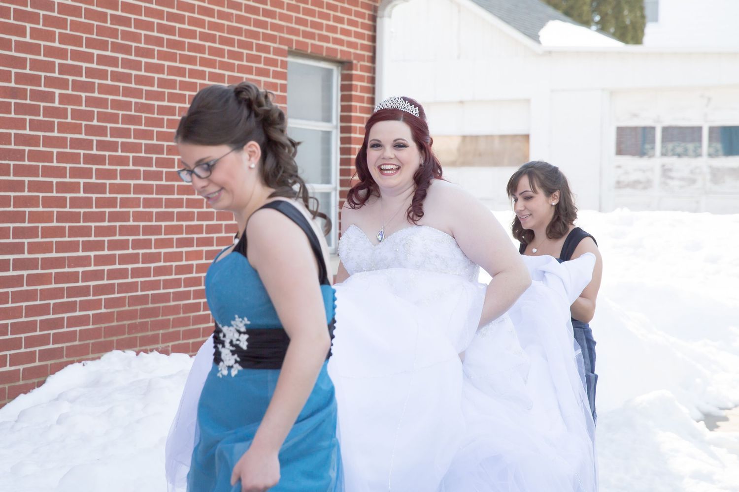 Bride in wedding gown walks through snow with bridesmaids wearing blue dresses.
