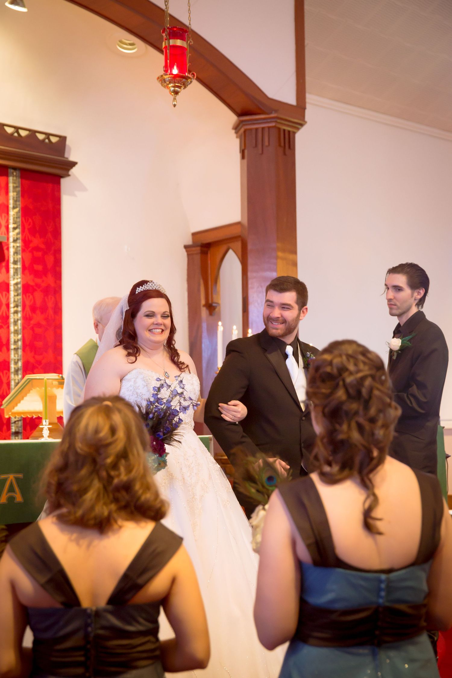 Wedding ceremony in church with bridesmaids in dark dresses watching.