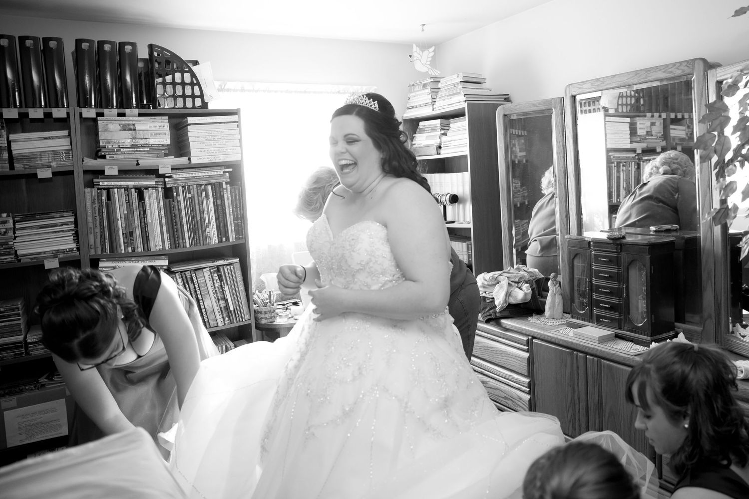 A bride in a strapless wedding gown laughs during preparations.