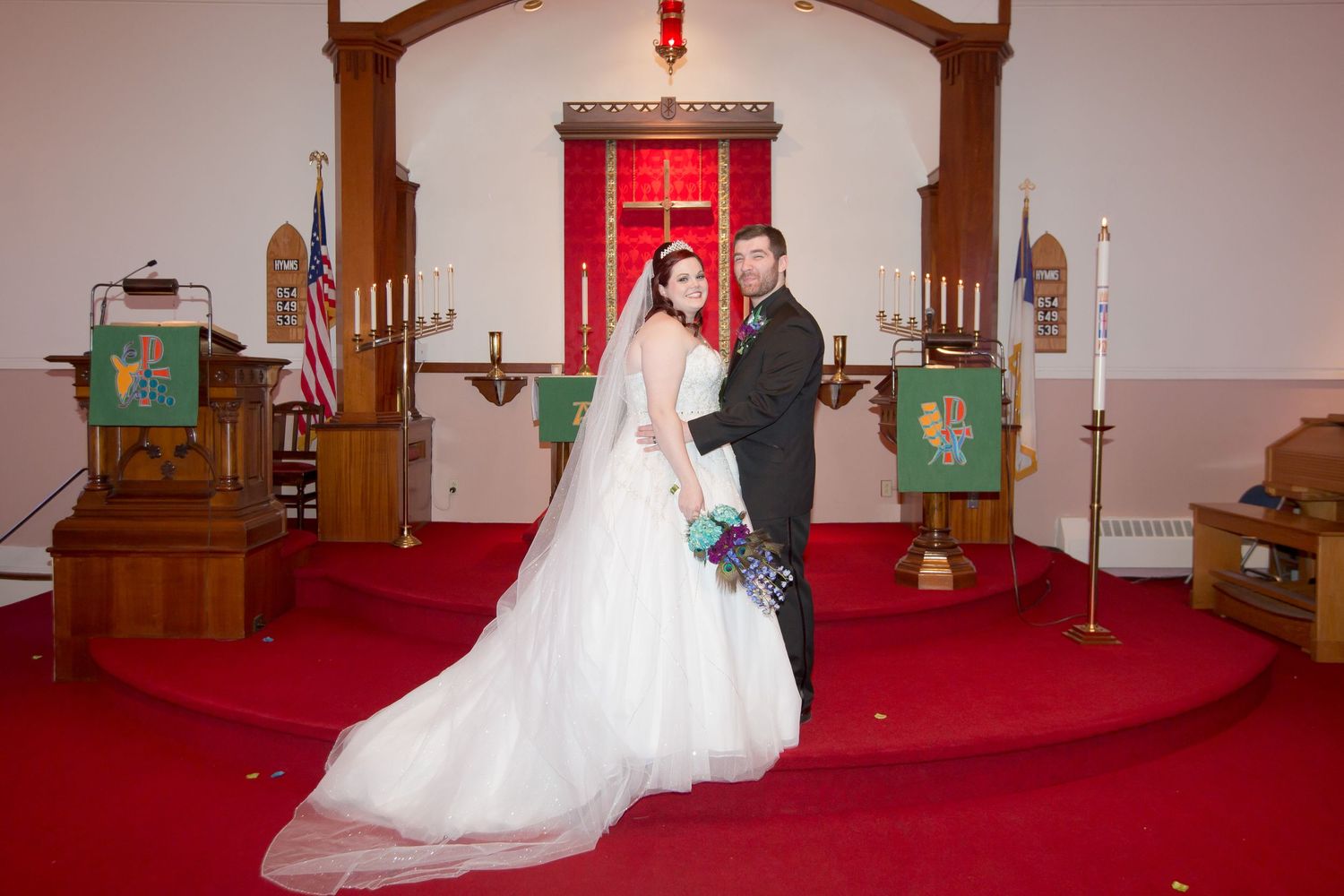Wedding couple poses in traditional church with red carpet and wooden archway.