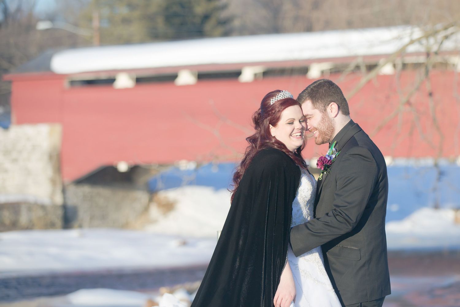 Winter wedding portrait with a red covered bridge in the background and couple in formal attire.