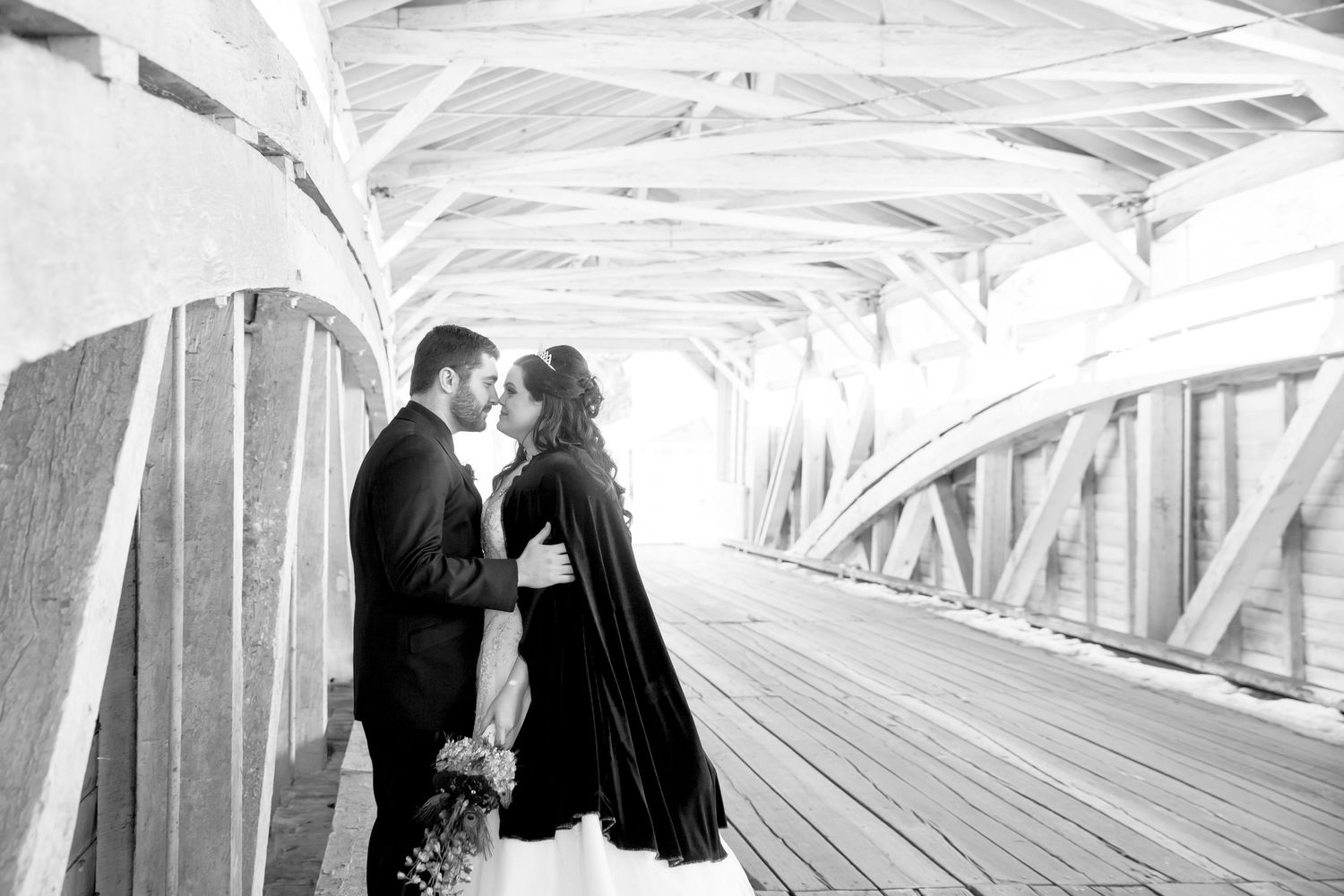 Black and white wedding portrait of a couple sharing an intimate moment in a covered bridge.