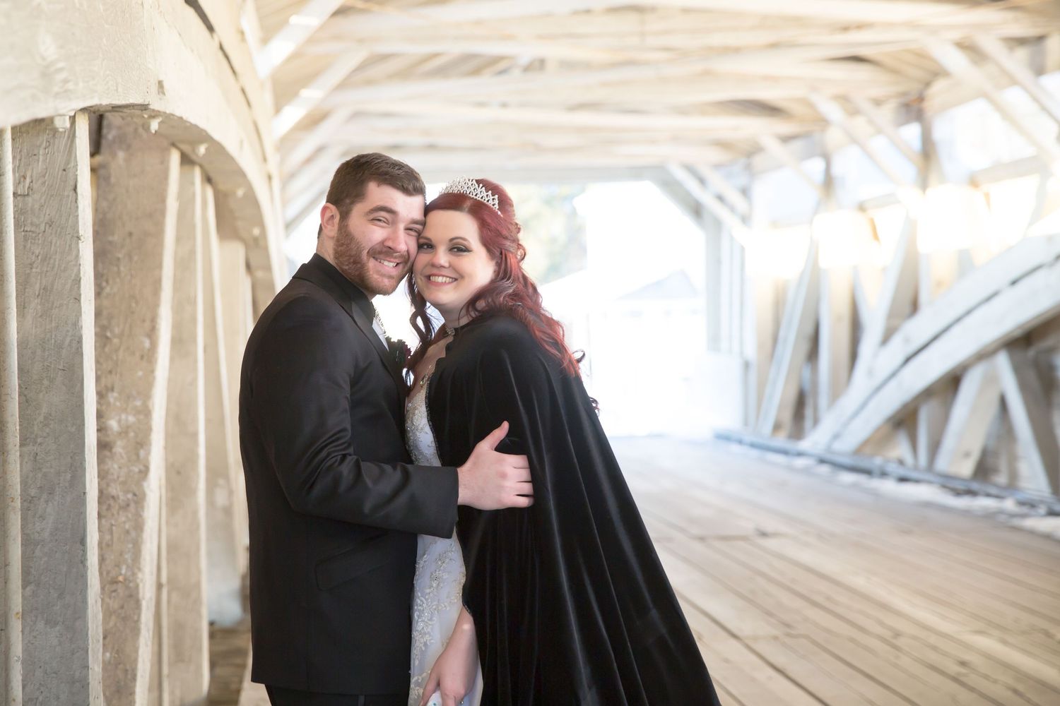 Intimate wedding photo of a couple embracing inside a rustic covered bridge with natural lighting.