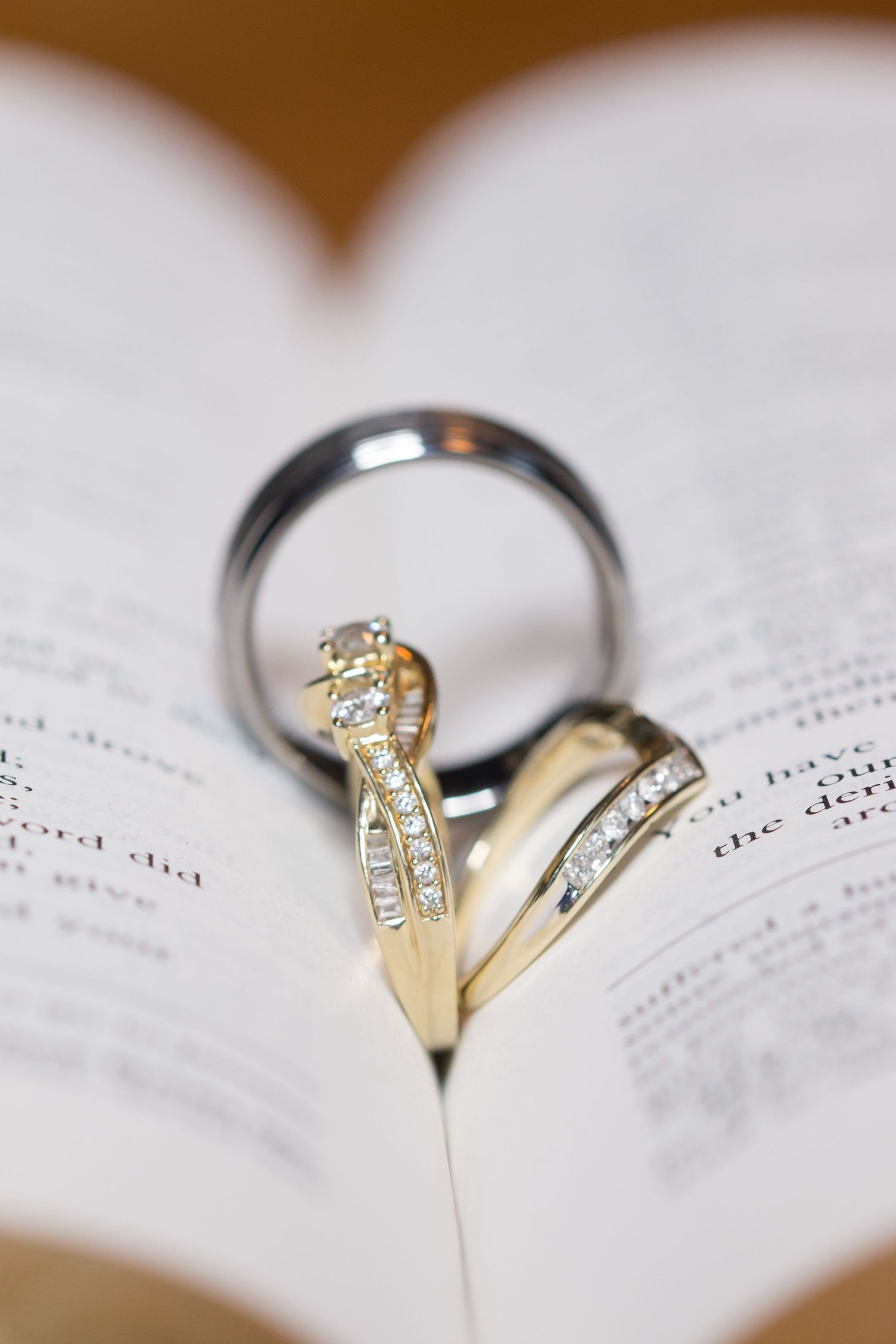 Wedding rings nestled in book pages, with one gold diamond ring and one silver band.