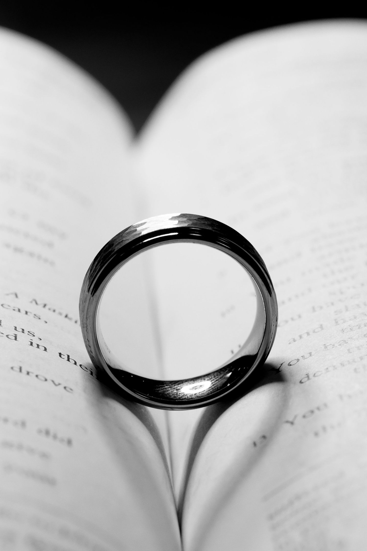 A silver wedding band creates a heart shadow on open book pages.