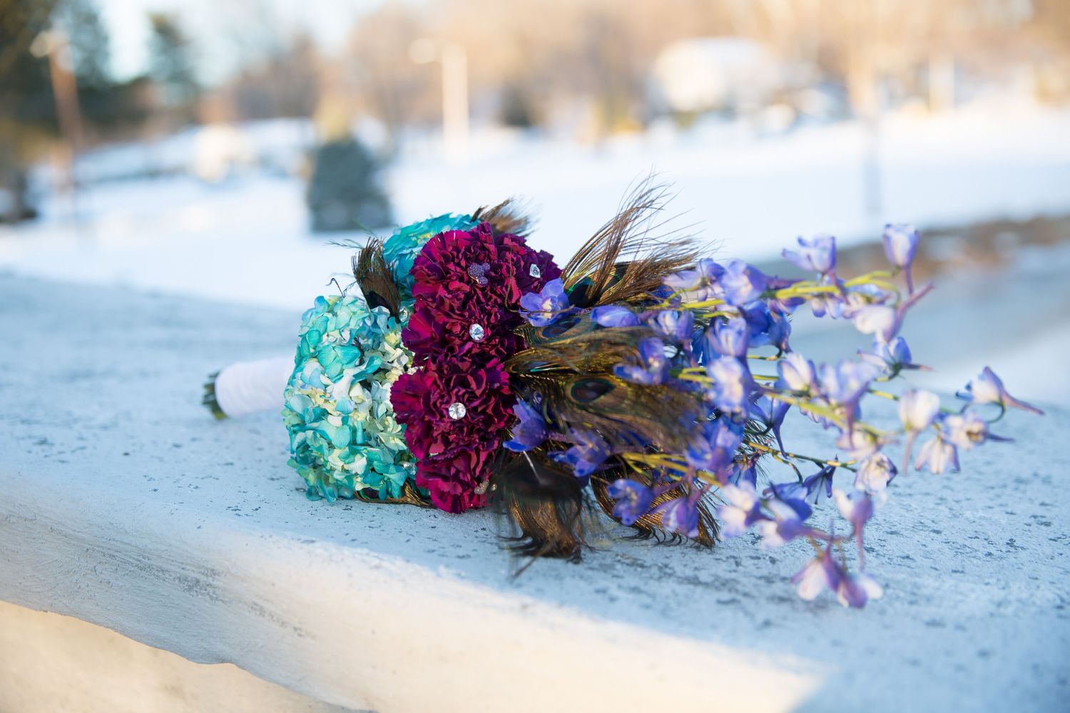 Wedding bouquet with turquoise and purple flowers resting in snow.