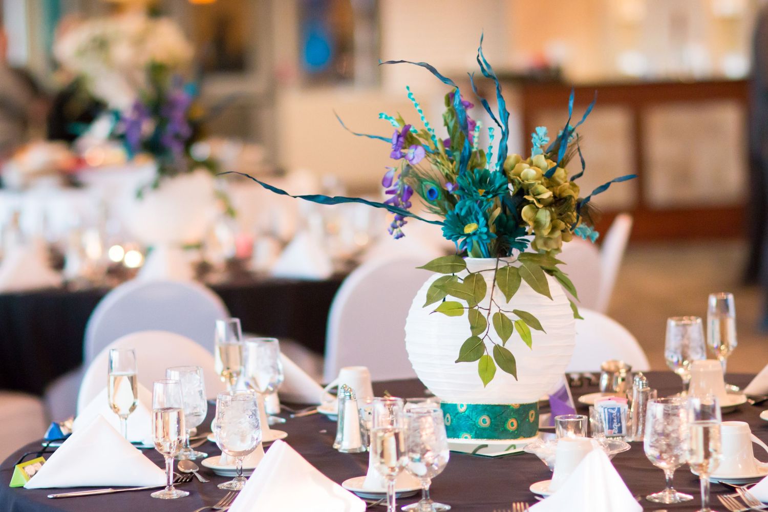 Elegant table setting with blue and teal floral centerpiece in a bright reception hall.