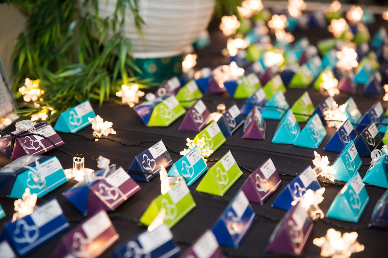 Colorful origami paper cranes arranged on dark surface with twinkling star lights in background.