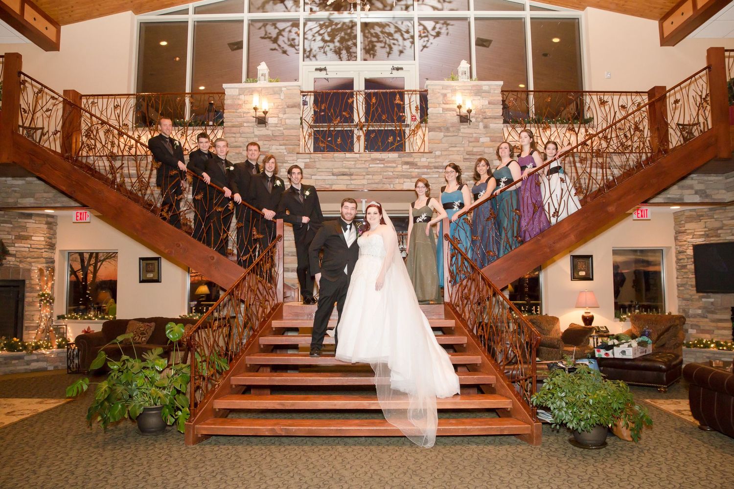 Wedding party members line grand wooden staircases while newlyweds pose in the center.