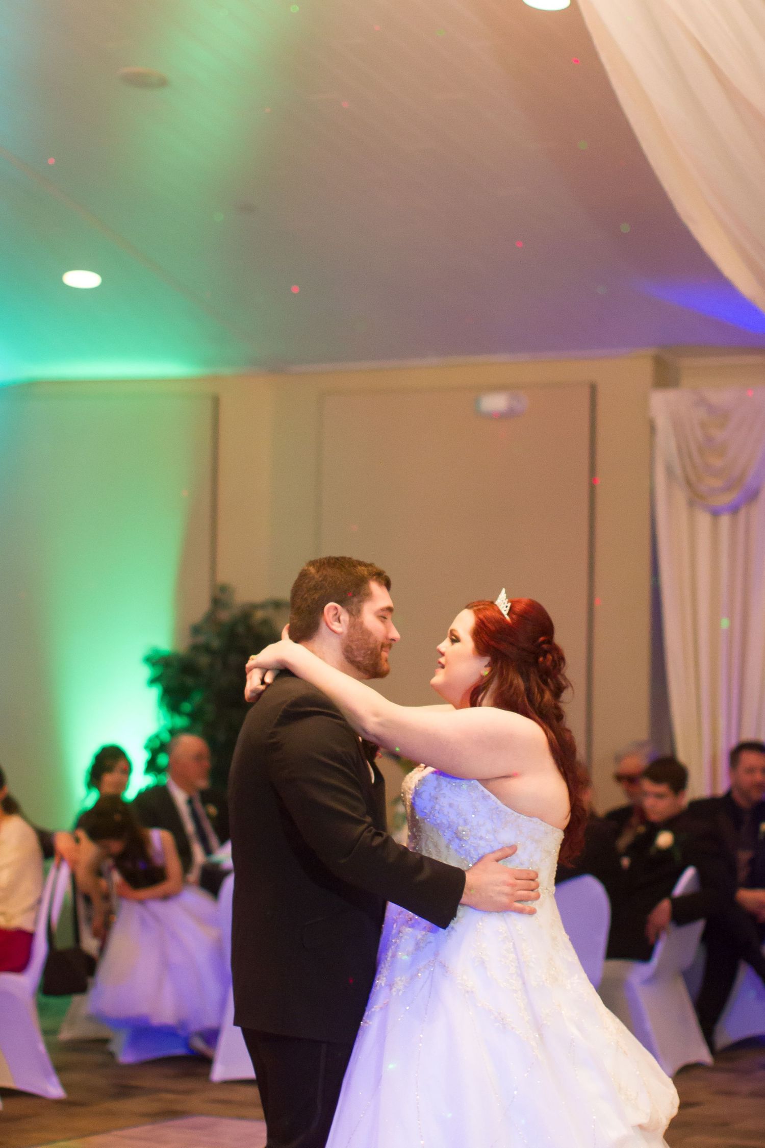 A romantic dance between newlyweds in a ballroom with ambient green and blue lighting.