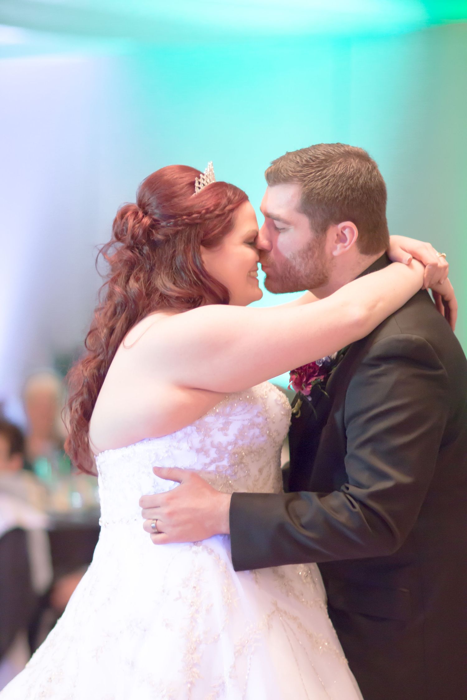 A tender moment between newlyweds dancing together under turquoise mood lighting.