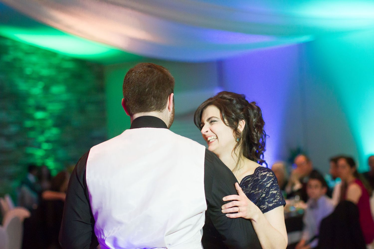 A couple shares an intimate dance moment under colorful blue and green lighting at a wedding reception.
