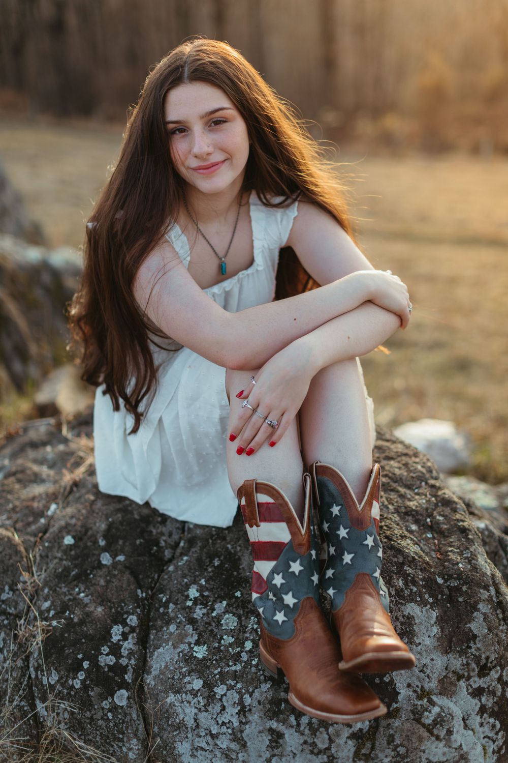 Person in white top sitting on rocky outcrop wearing decorative boots at sunset.