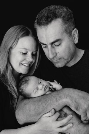 Black and white portrait of new parents tenderly holding their sleeping newborn.