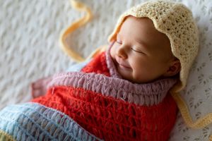 Sleeping newborn wearing a red sweater and cream colored knit bonnet.