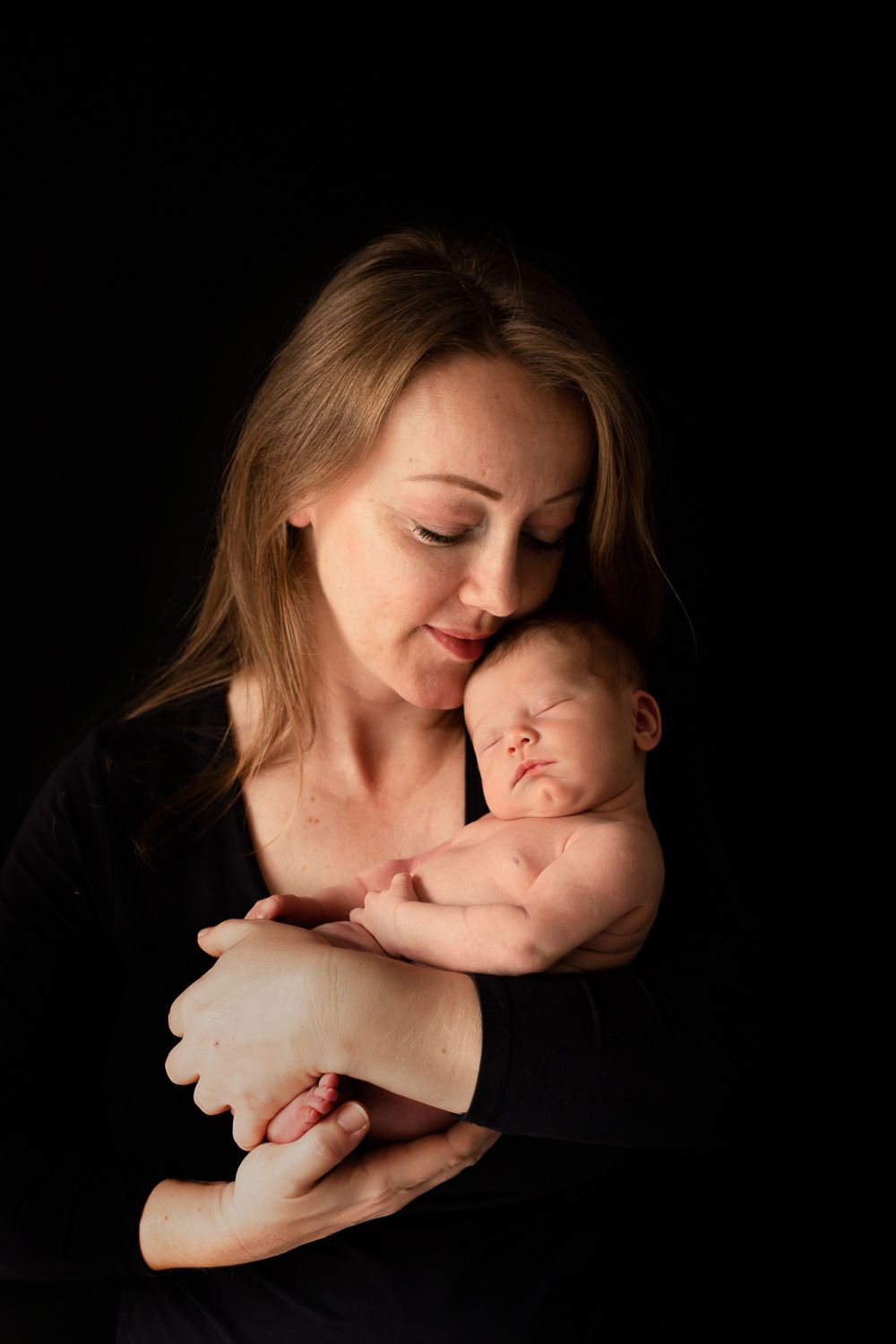 Dramatic portrait of mother and baby against black background.