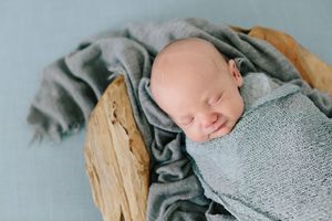 A peaceful sleeping newborn baby wrapped in soft gray swaddle on wooden surface.