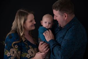 An intimate family portrait against dark background showing parents with their baby.