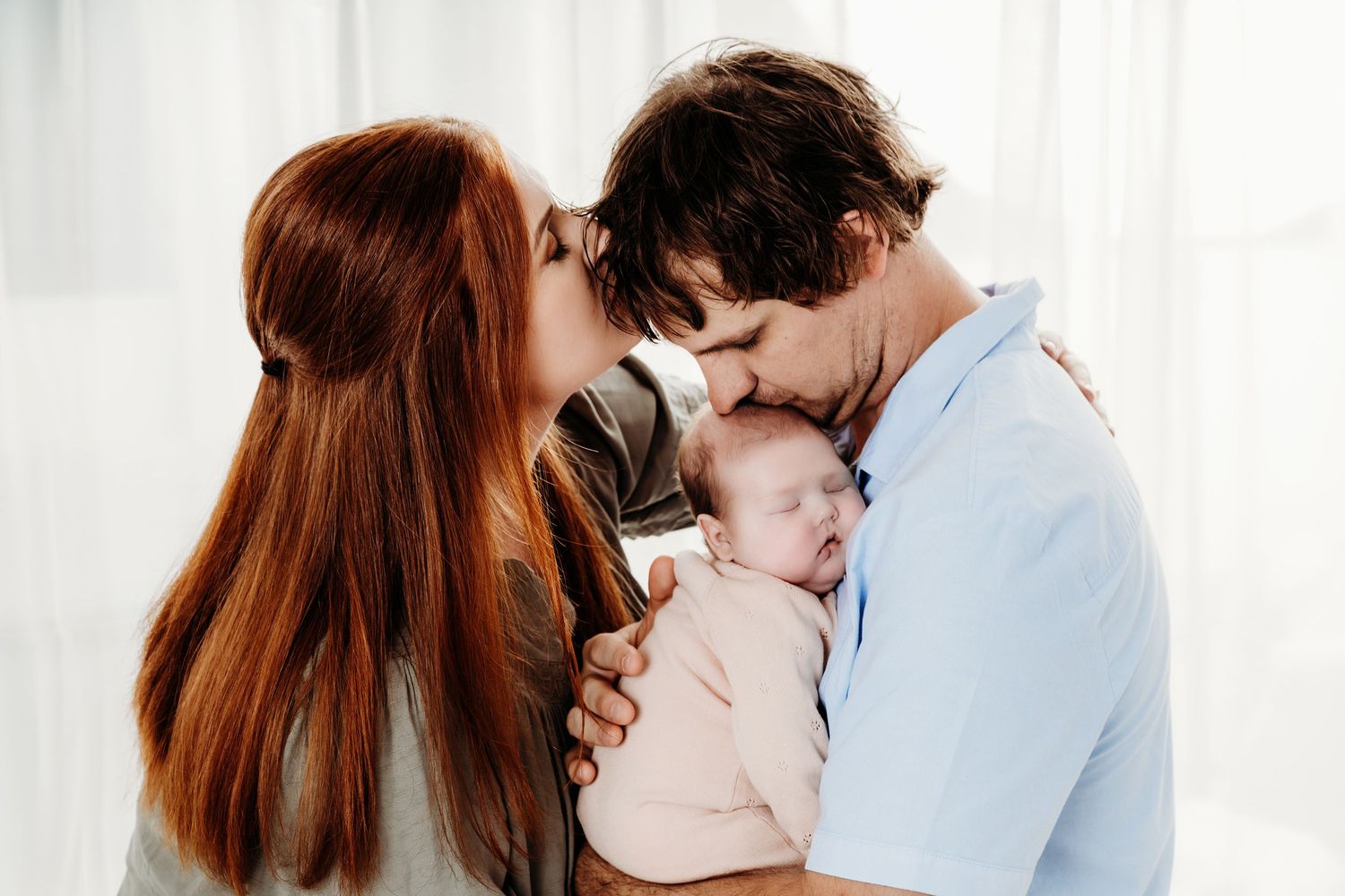 A tender family moment as parents share a special kiss while holding their newborn baby.